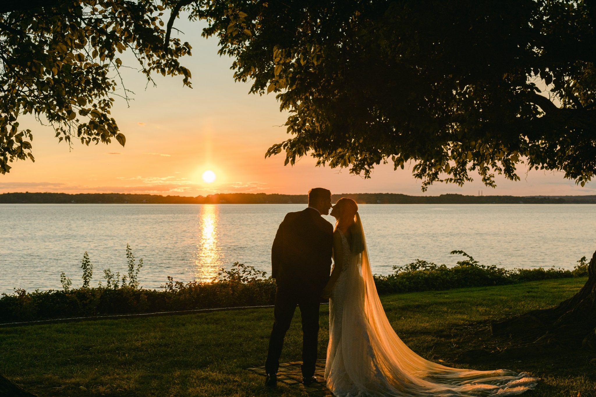 Bride and Groom kiss on waterfront at sunset